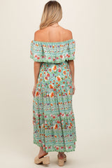 woman wearing a floral green off-the-shoulder maternity dress with a flowing skirt, showing her back