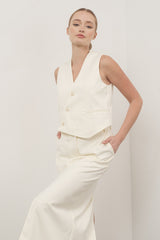 woman wearing an off-white sleeveless double-breasted vest with side pockets and matching high-waisted pants