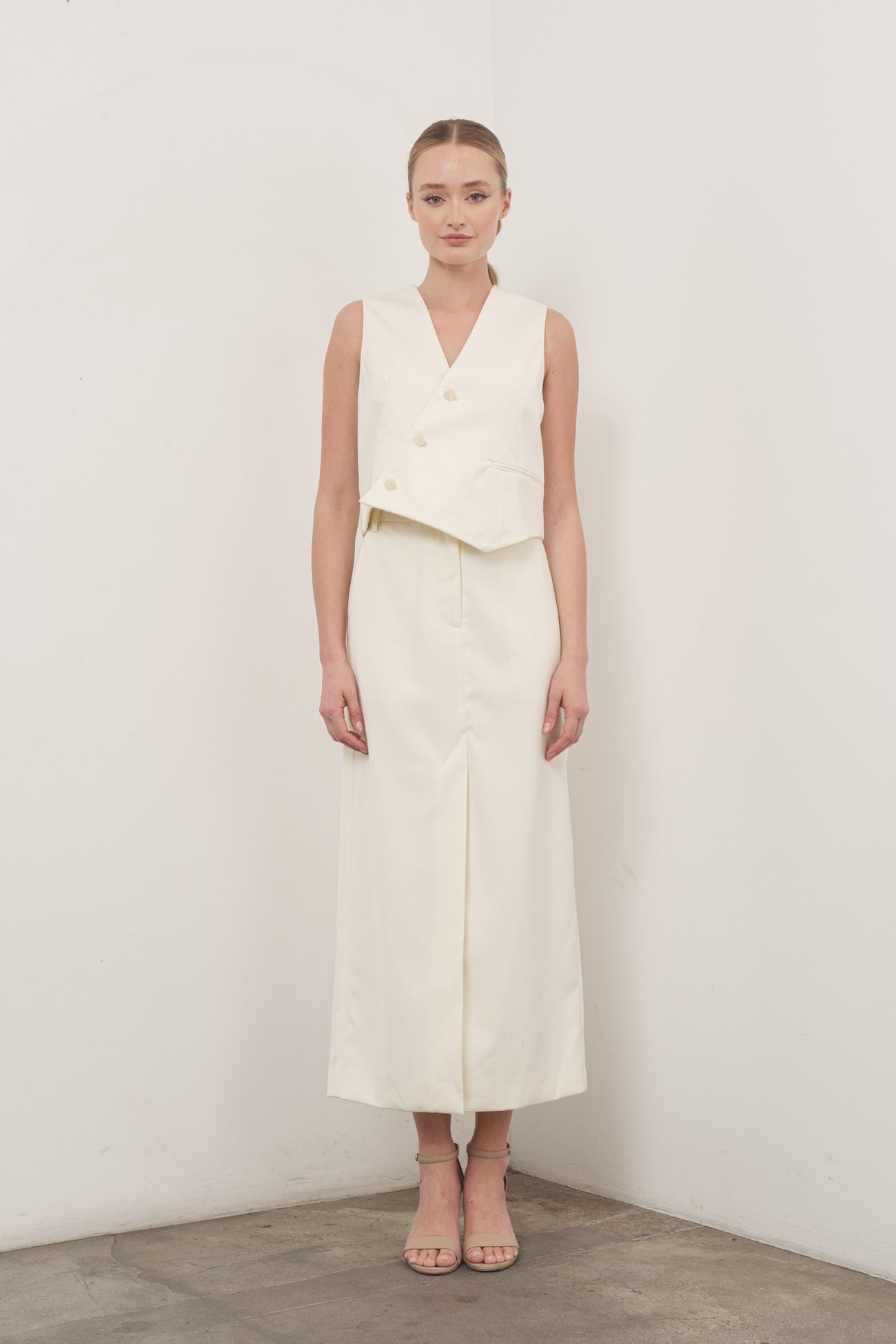woman wearing a cream sleeveless cropped vest and a matching long skirt with a front slit