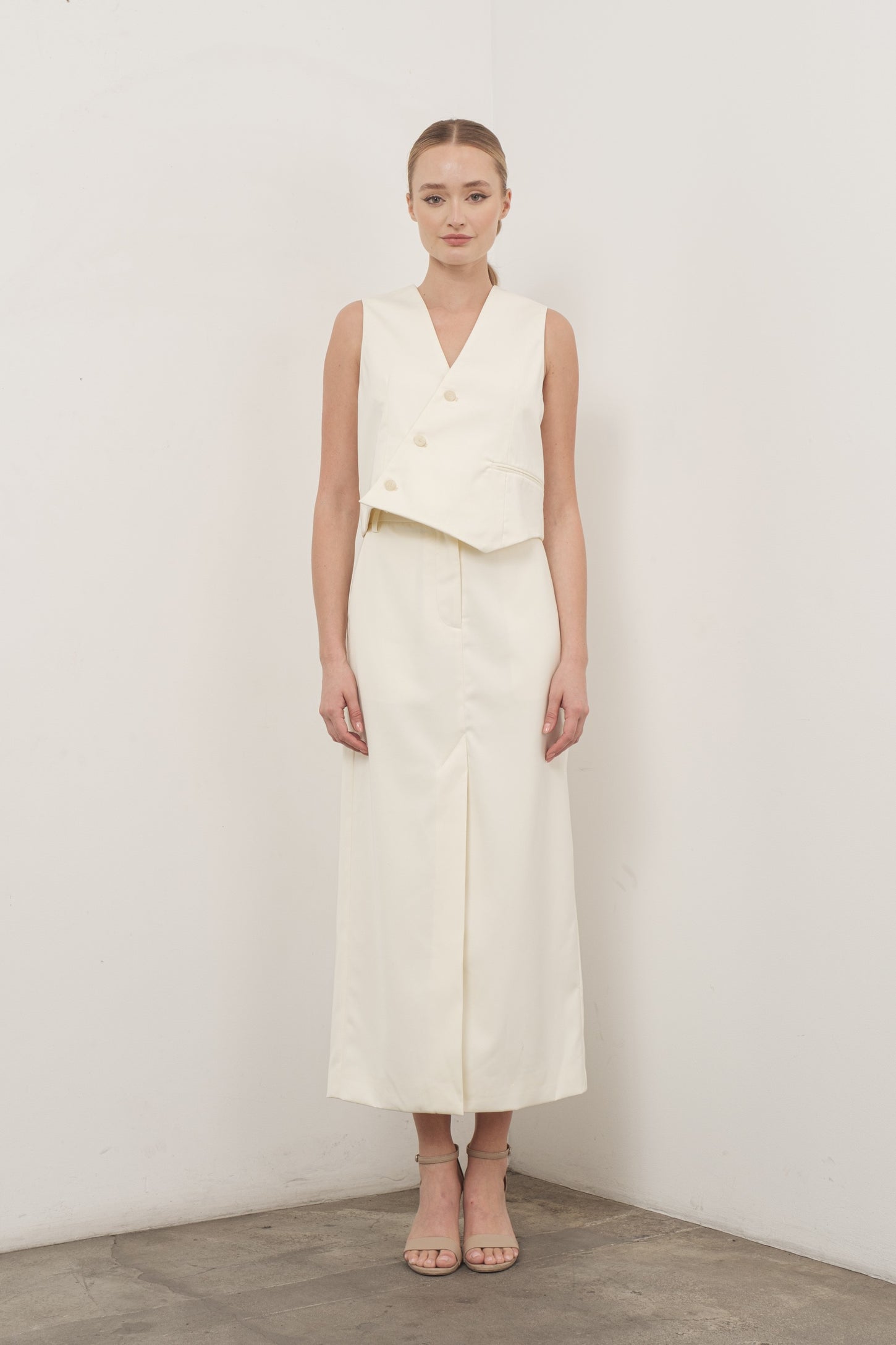 woman wearing a cream sleeveless cropped vest and a matching long skirt with a front slit
