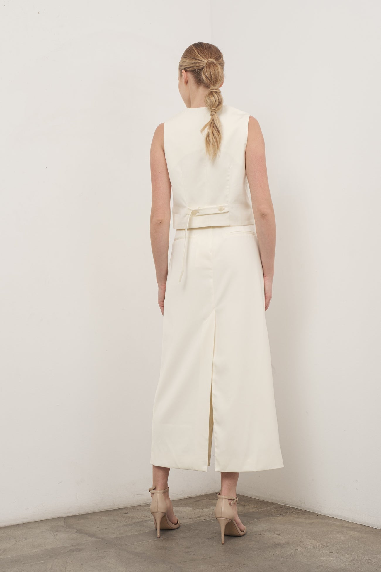 woman wearing a cream sleeveless dress with a back tie detail and a high slit, styled with strappy heels