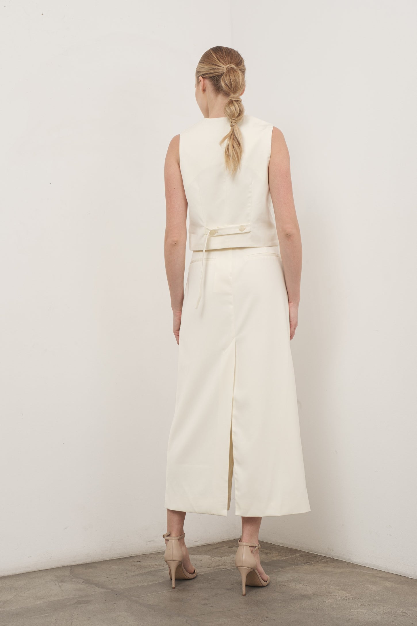 woman wearing a cream sleeveless dress with a back tie detail and a high slit, styled with strappy heels