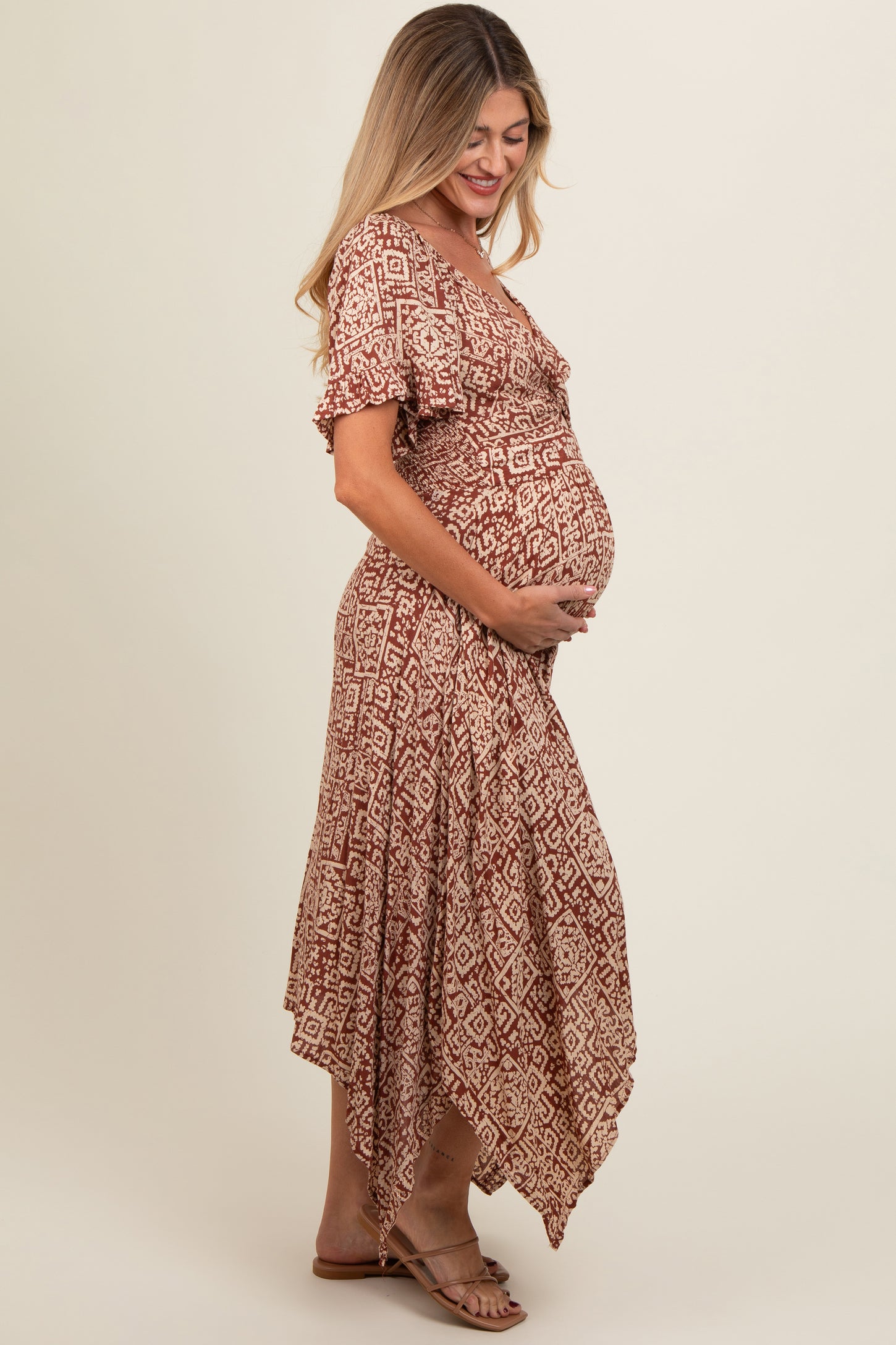 woman wearing a rust patterned maternity dress with a high-low hem and holding her baby bump
