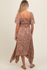 woman wearing a brown patterned maternity dress with a smocked bodice and high-low hem, showing a baby bump