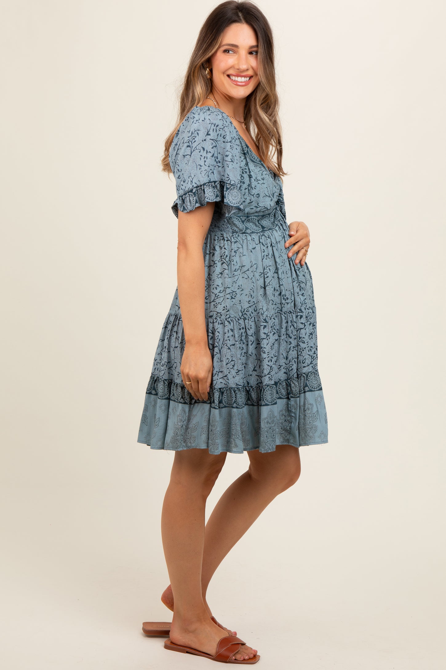 woman wearing a light blue floral maternity dress and holding her baby bump