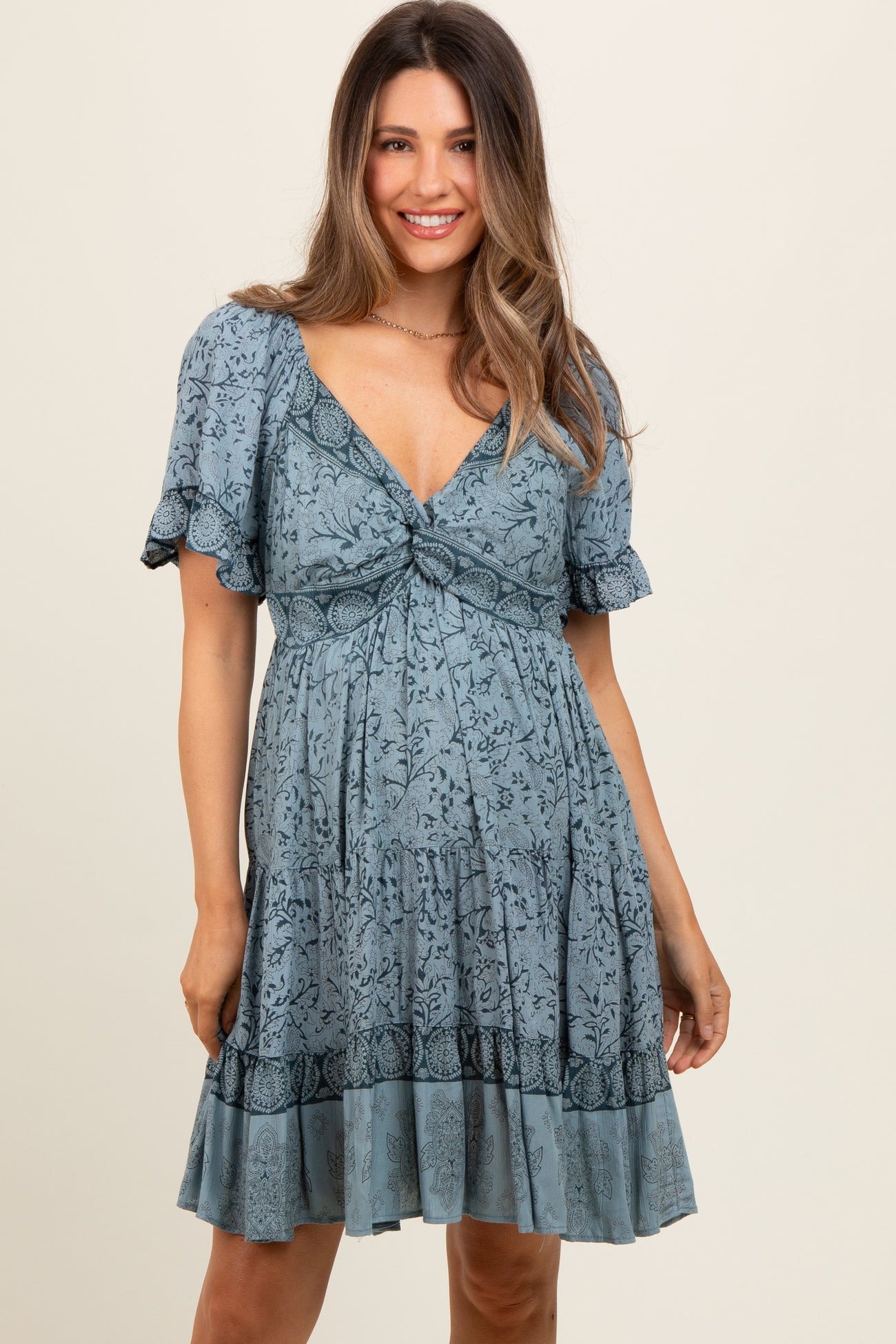 woman wearing a blue floral print maternity dress with short sleeves and a gathered waist, showcasing a baby bump