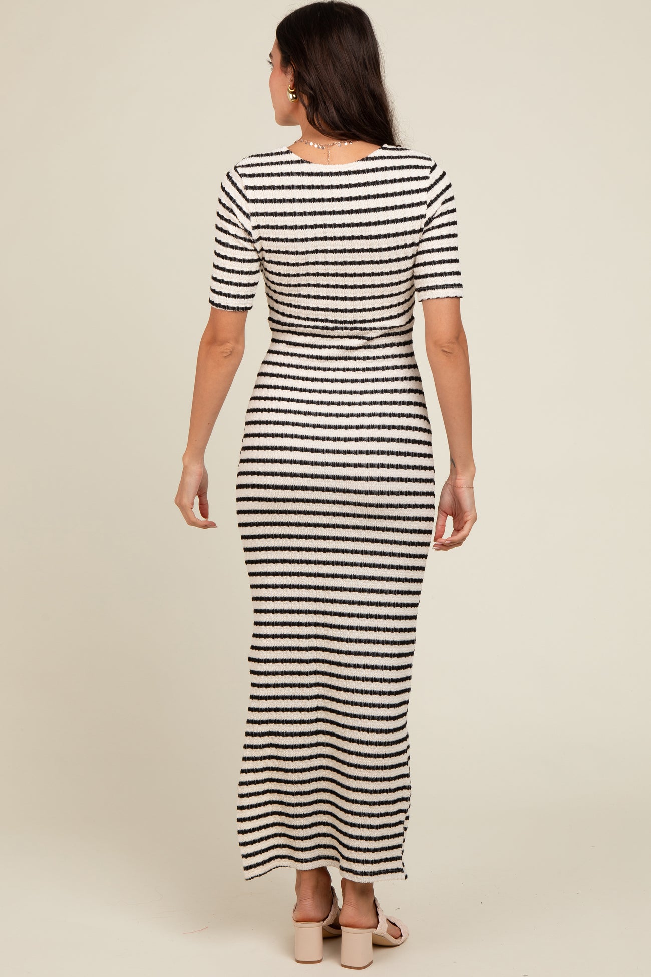 woman wearing a striped maxi dress with short sleeves, seen from the back on a neutral background