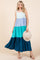 woman wearing a color-blocked maxi dress in mint, lavender, teal, and navy, holding a wide-brimmed straw hat