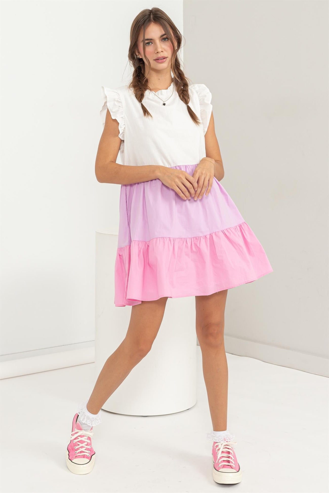 woman wearing a white and pink color-blocked dress with ruffle sleeves and a tiered skirt, paired with pink sneakers