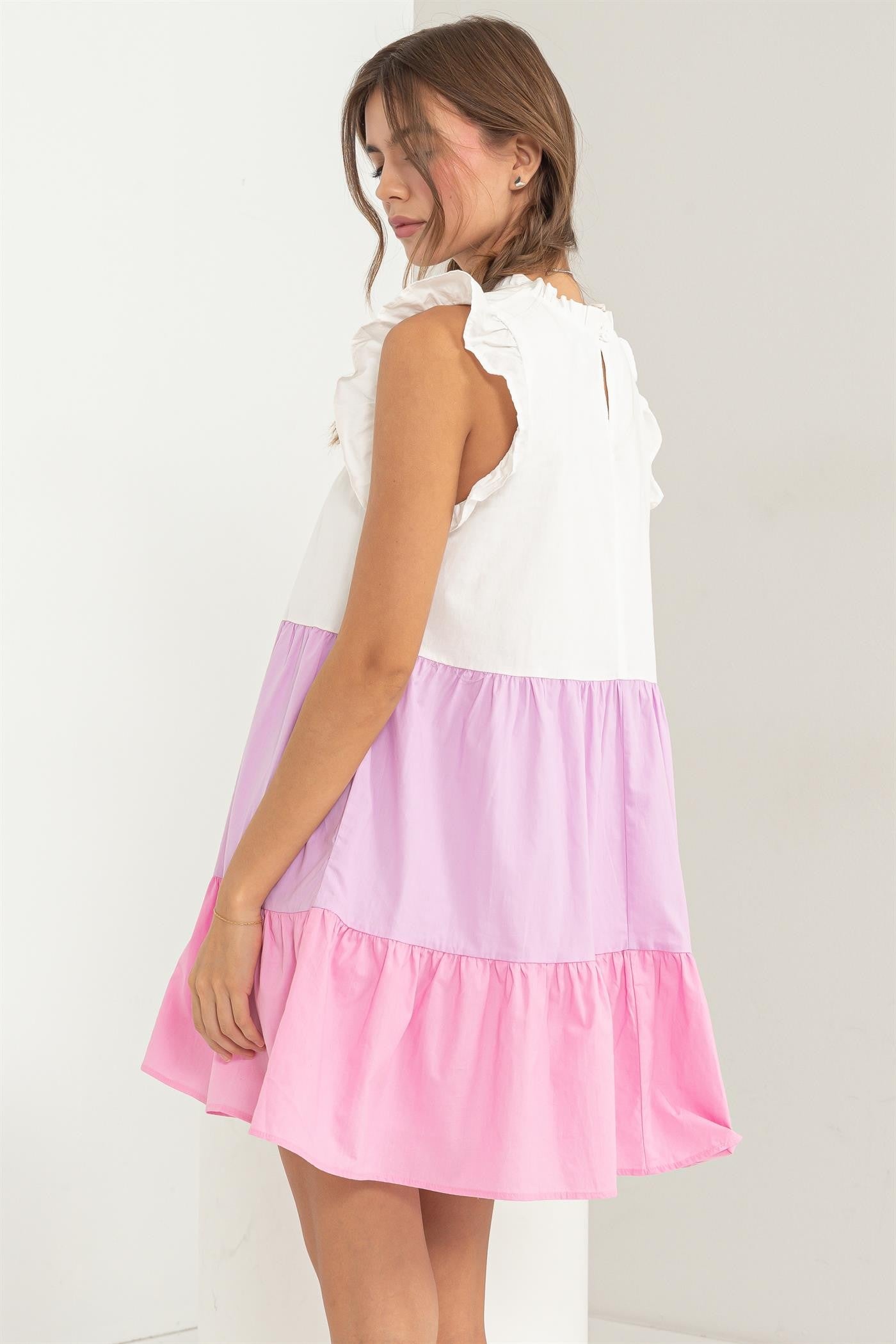 woman wearing a white, pink, and lavender color-blocked sleeveless dress with ruffle details and a tiered hem