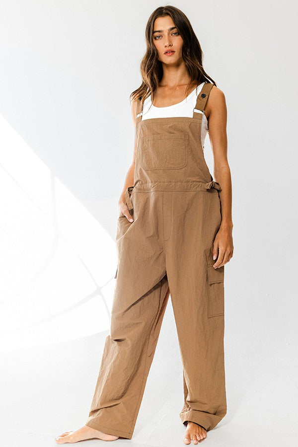 woman wearing a brown overall jumpsuit with side pockets and adjustable straps, styled casually without shoes