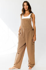 woman wearing a brown overall jumpsuit with side pockets and adjustable straps, styled casually without shoes