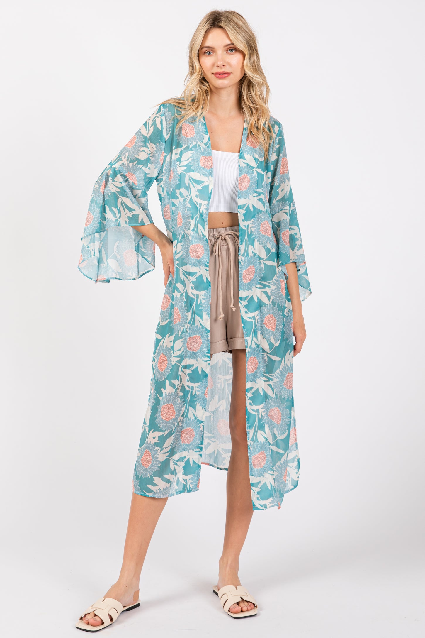 woman wearing a light blue floral kimono over a white crop top and beige shorts, standing on a white background