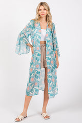 woman wearing a light blue floral kimono over a white crop top and beige shorts, standing on a white background