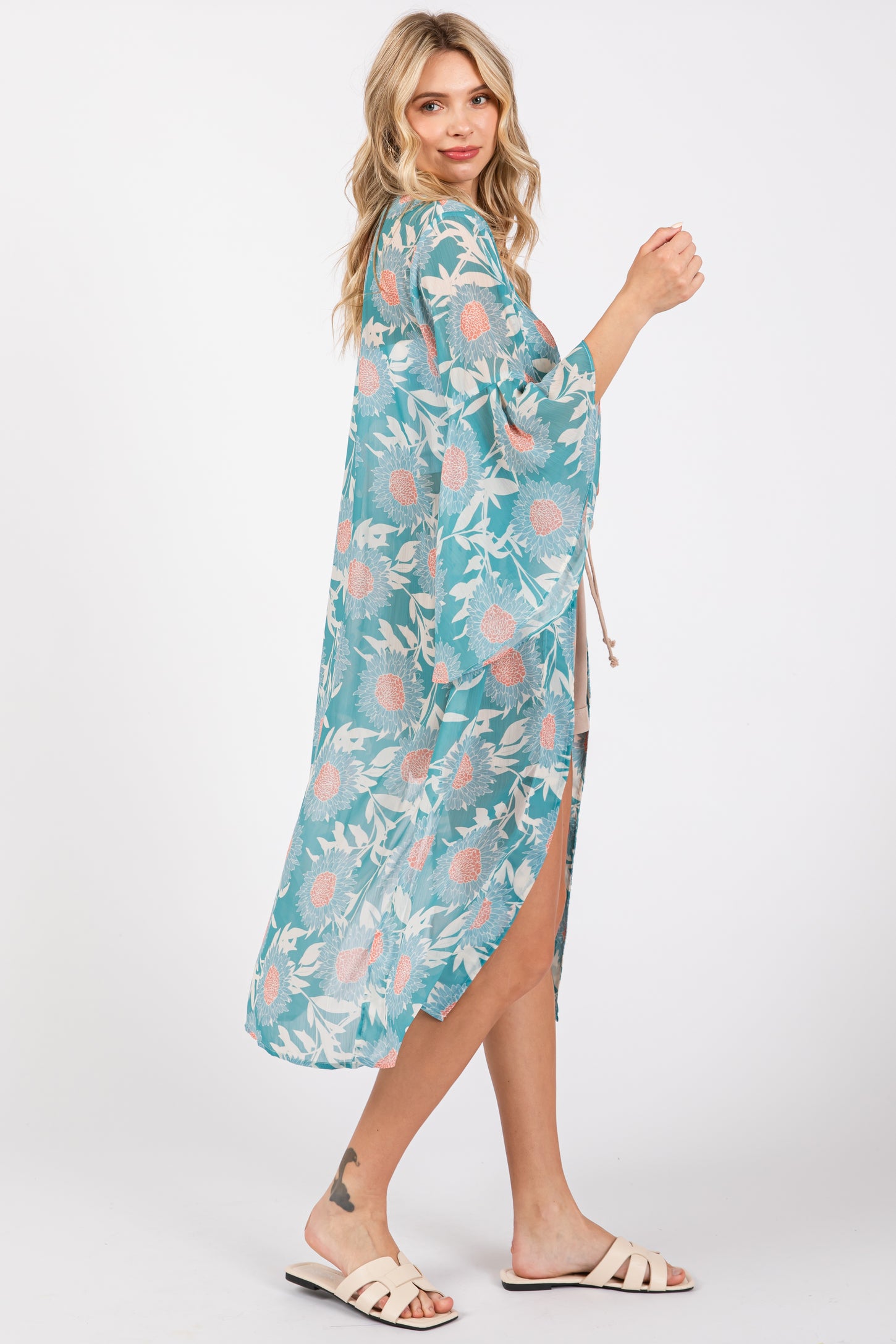 woman wearing a teal floral kimono with open sides and a tie waist, styled over a casual outfit