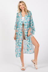 woman wearing a turquoise floral kimono over a white crop top and beige shorts, standing in a casual pose