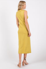 woman wearing a sleeveless mustard yellow midi dress, standing with her back to the camera, showing a simple design