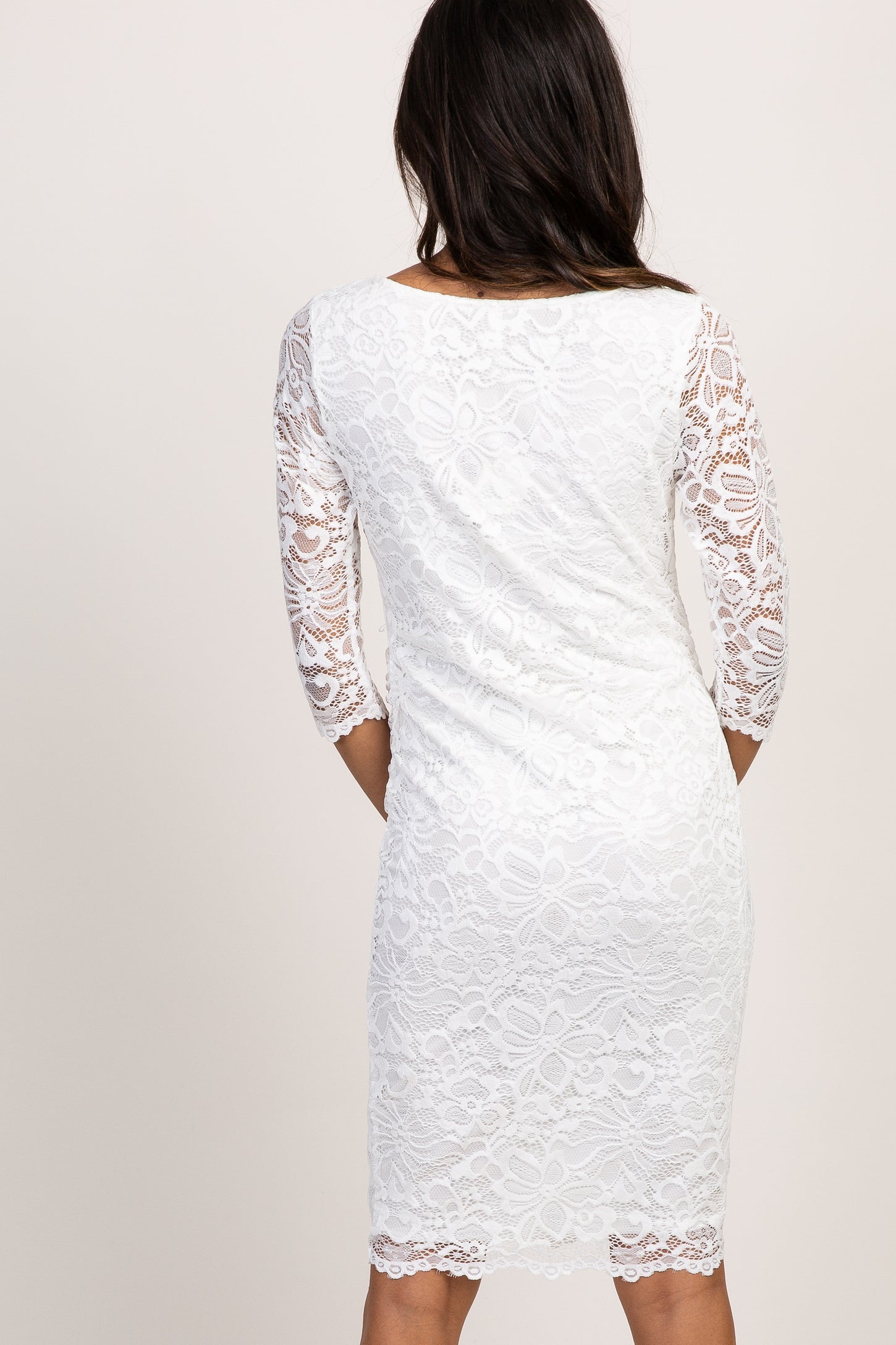 smiling pregnant woman in white lace maternity dress standing in front of rustic wooden doors