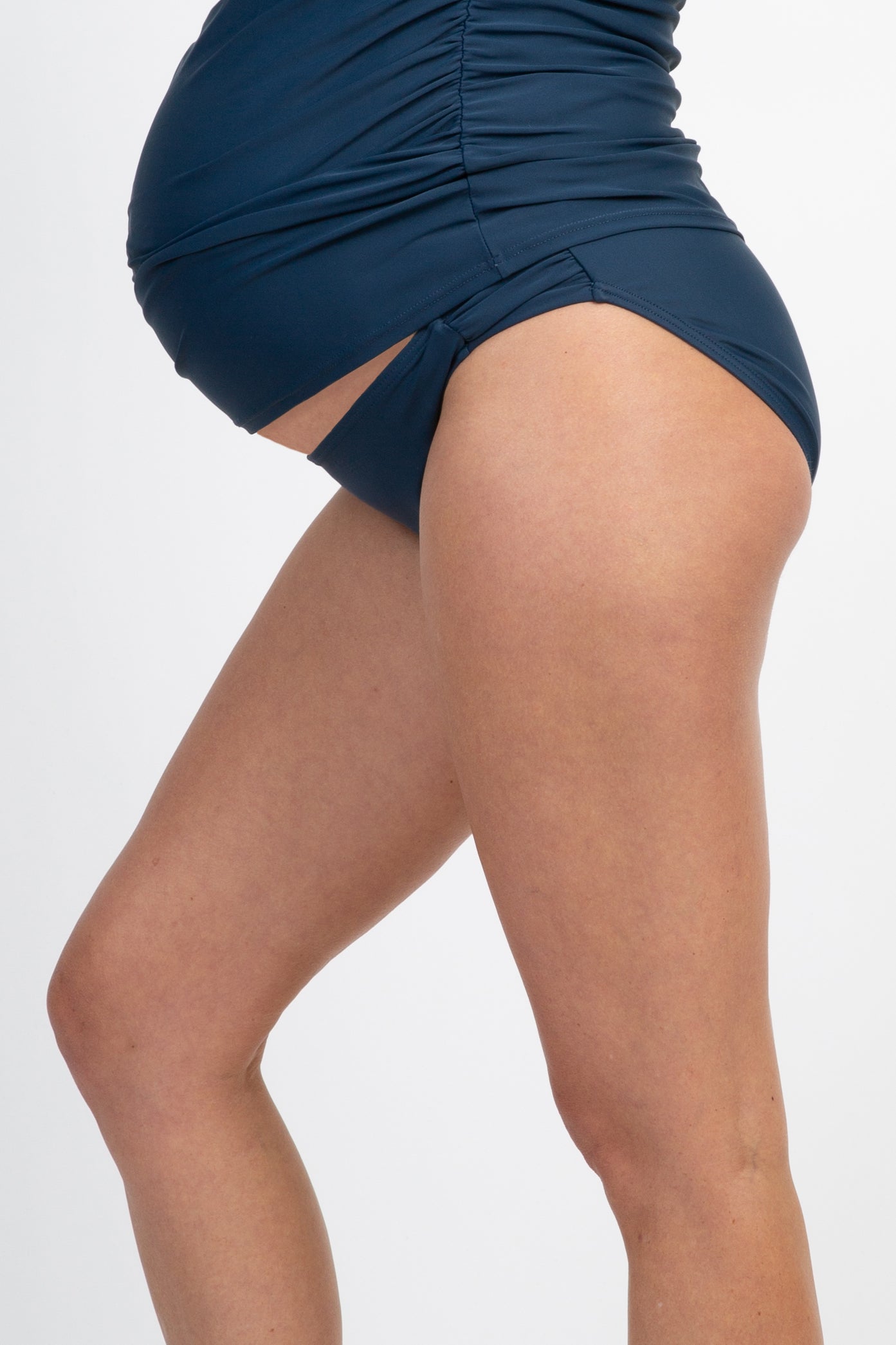 woman wearing a navy blue maternity swim bottom, featuring ruching and a snug fit around her baby bump