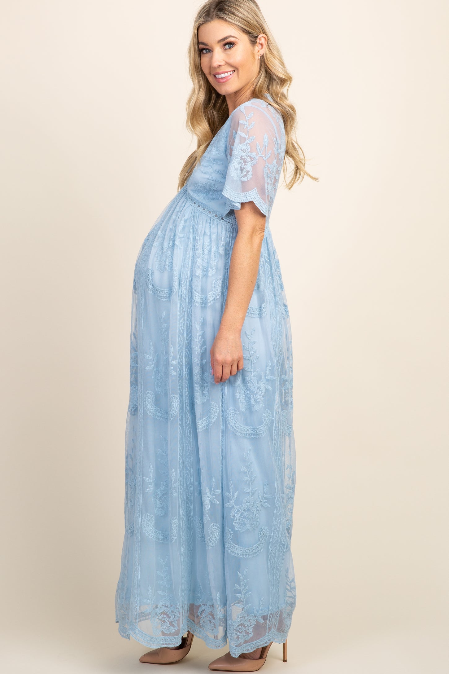 woman wearing a light blue maternity gown with floral embroidery and a visible baby bump