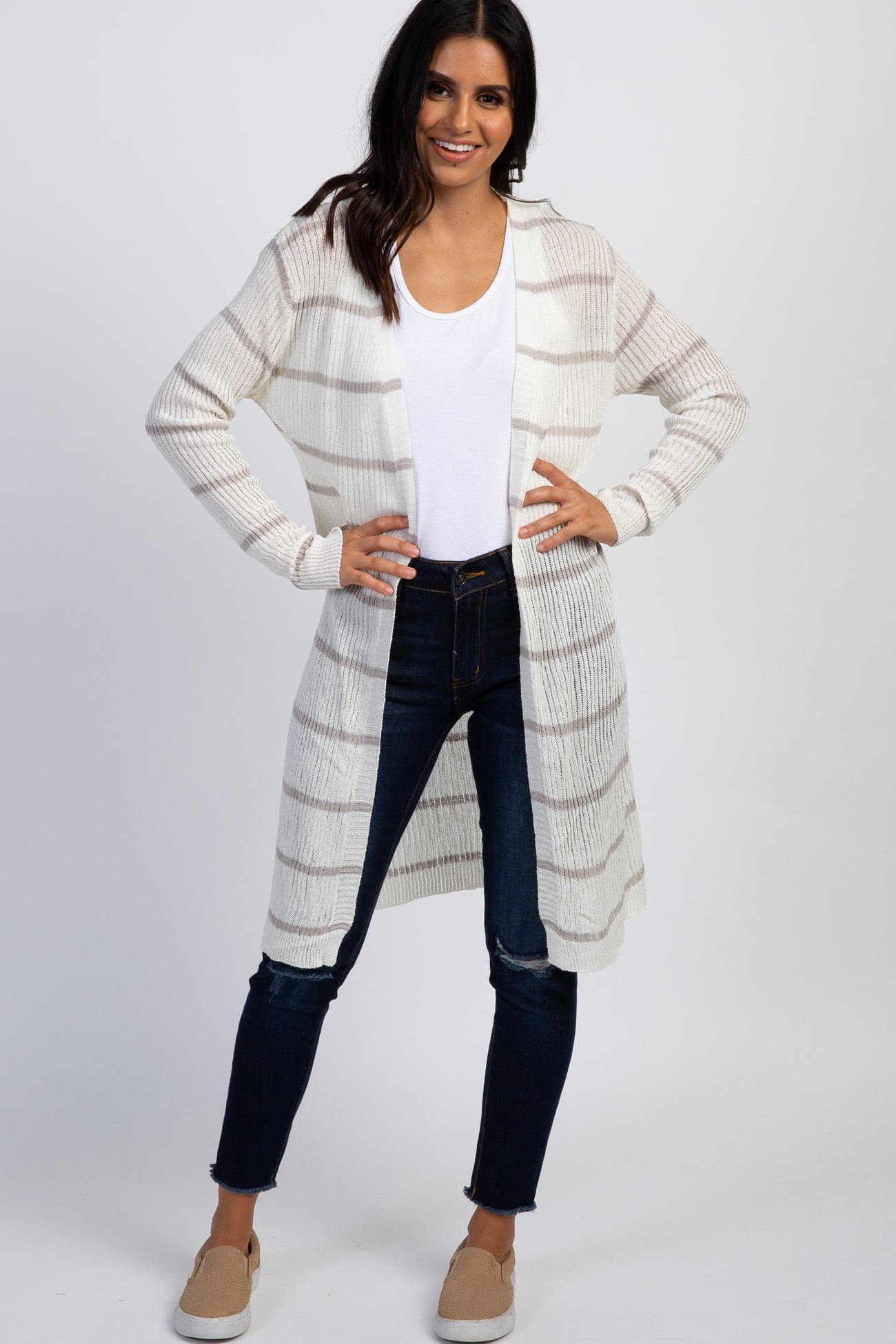 woman wearing a white and tan striped long cardigan with dark blue jeans and tan slip-on shoes