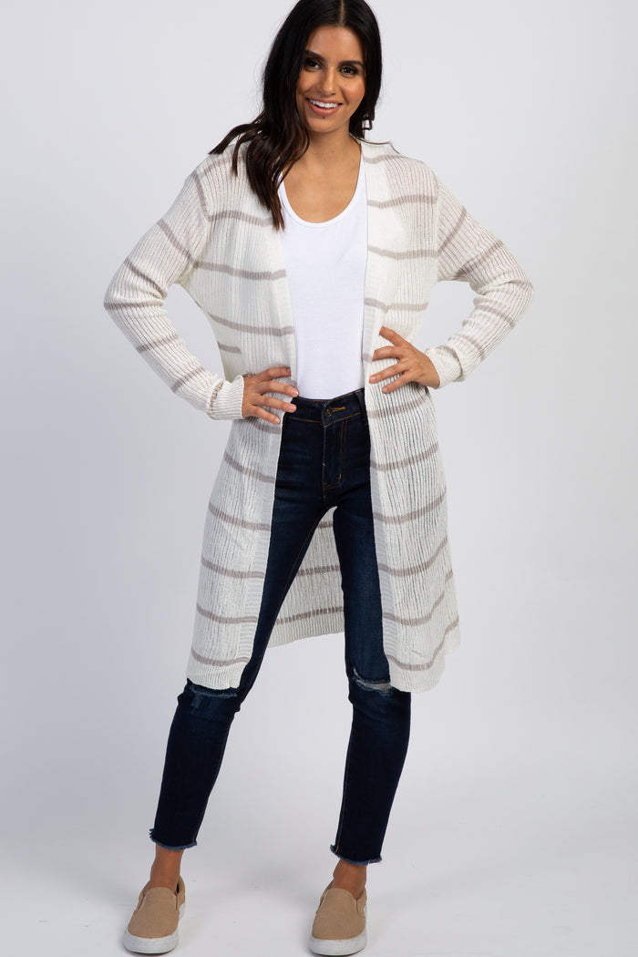 woman wearing a white and tan striped long cardigan with dark blue jeans and tan slip-on shoes