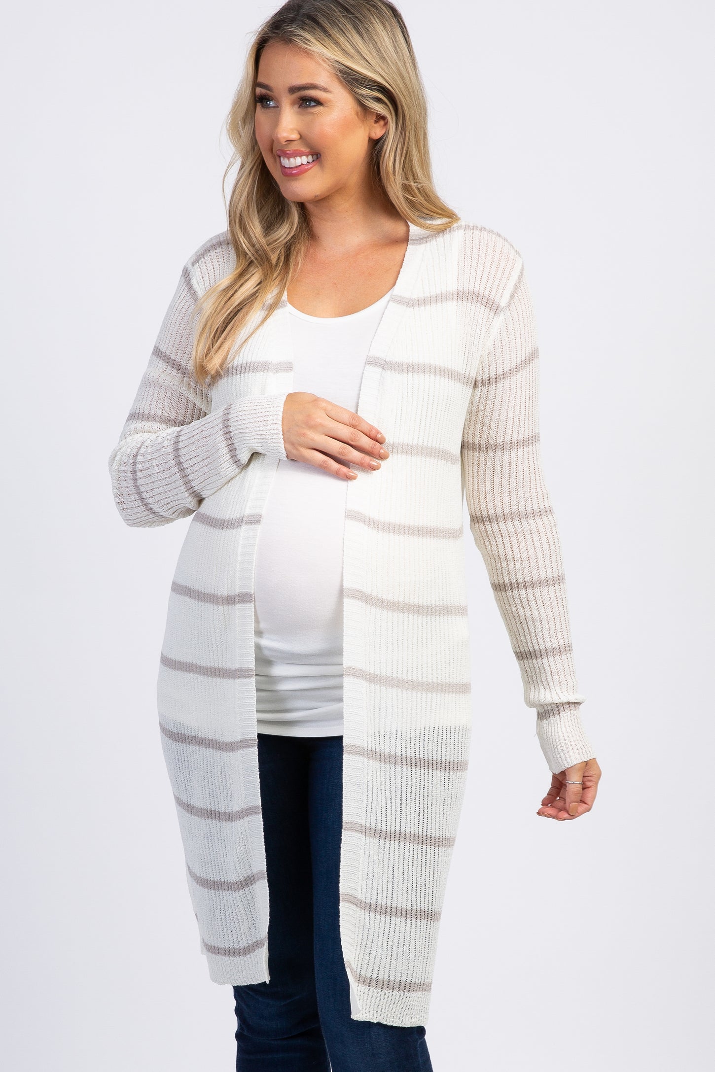 smiling pregnant woman wearing a white and grey striped long maternity cardigan over a white top and jeans