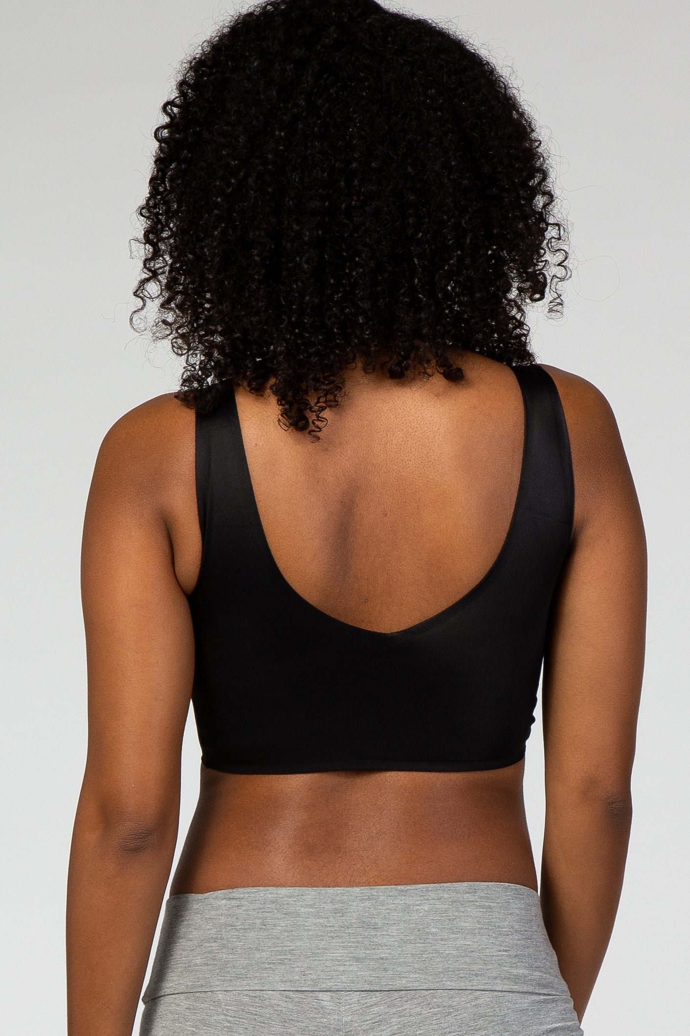Back view of a woman with curly hair wearing a black scoop neck sports bra and grey leggings