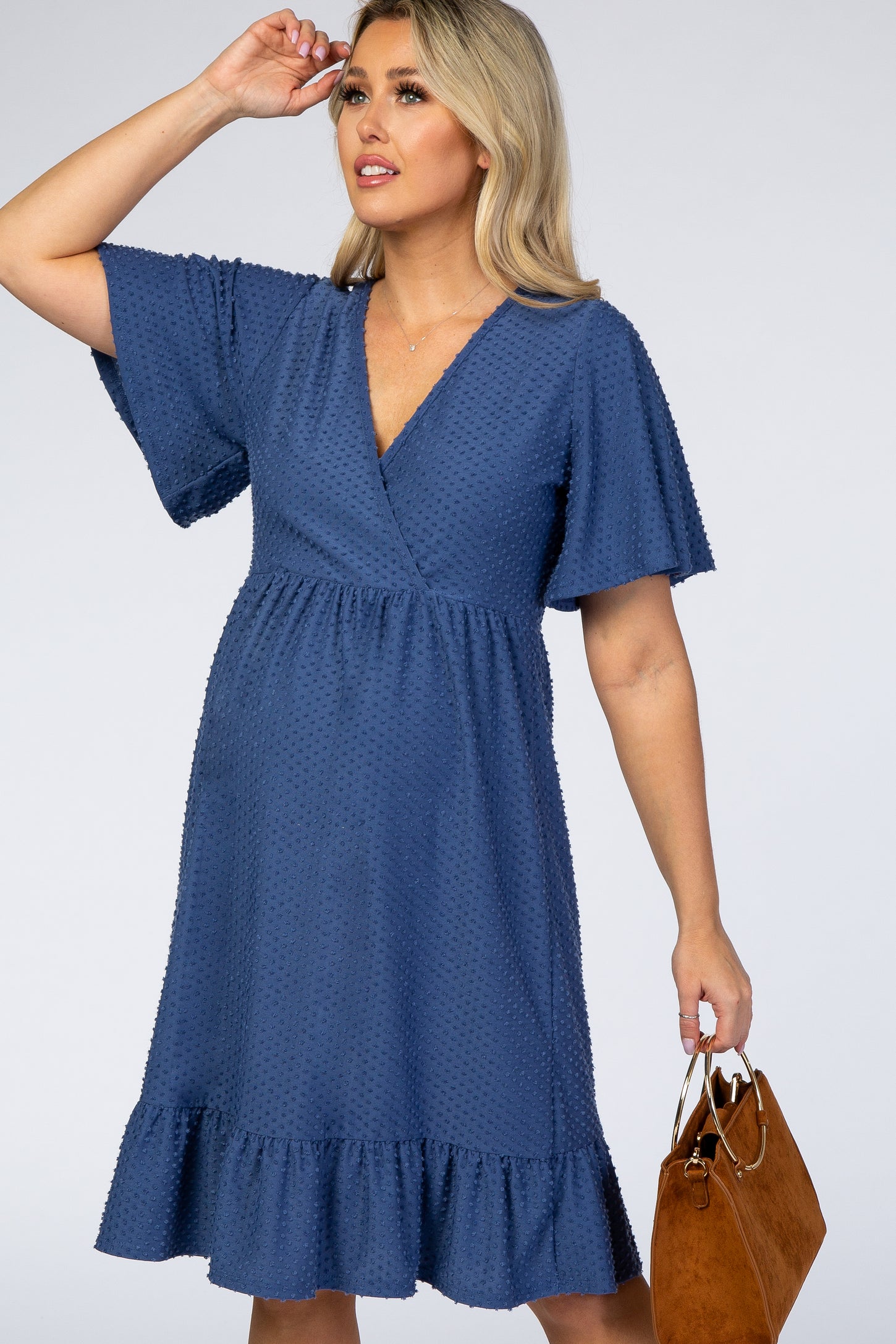 woman wearing a navy blue maternity wrap dress with flutter sleeves and a ruffled hem, holding a brown handbag