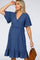 woman wearing a navy blue maternity wrap dress with flutter sleeves and a ruffled hem, holding a brown handbag
