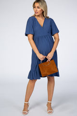 woman wearing a dark blue short sleeve maternity dress with ruffle hem and holding a tan handbag, showing her baby bump