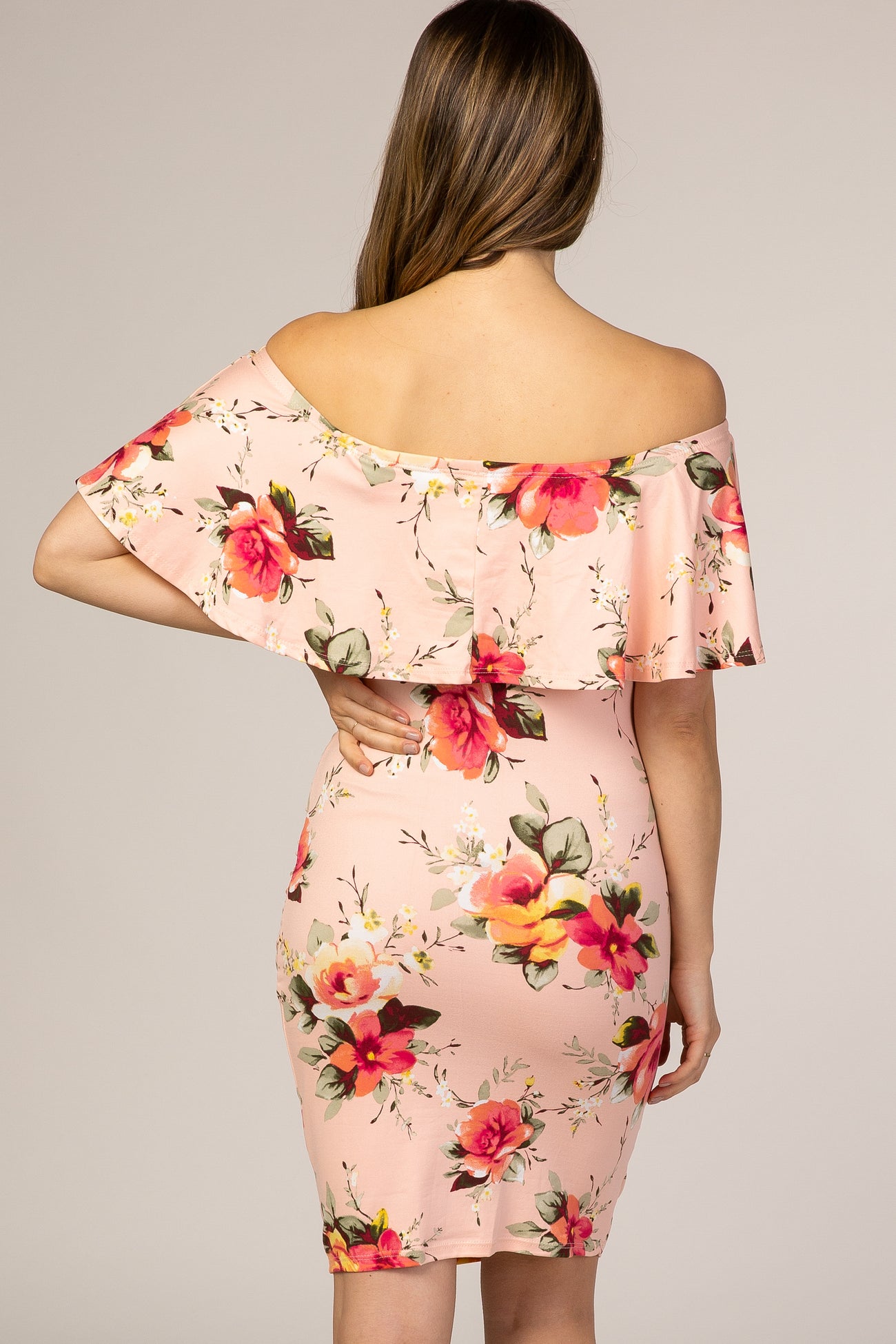 Back view of a woman wearing a light pink off-the-shoulder floral ruffle maternity dress