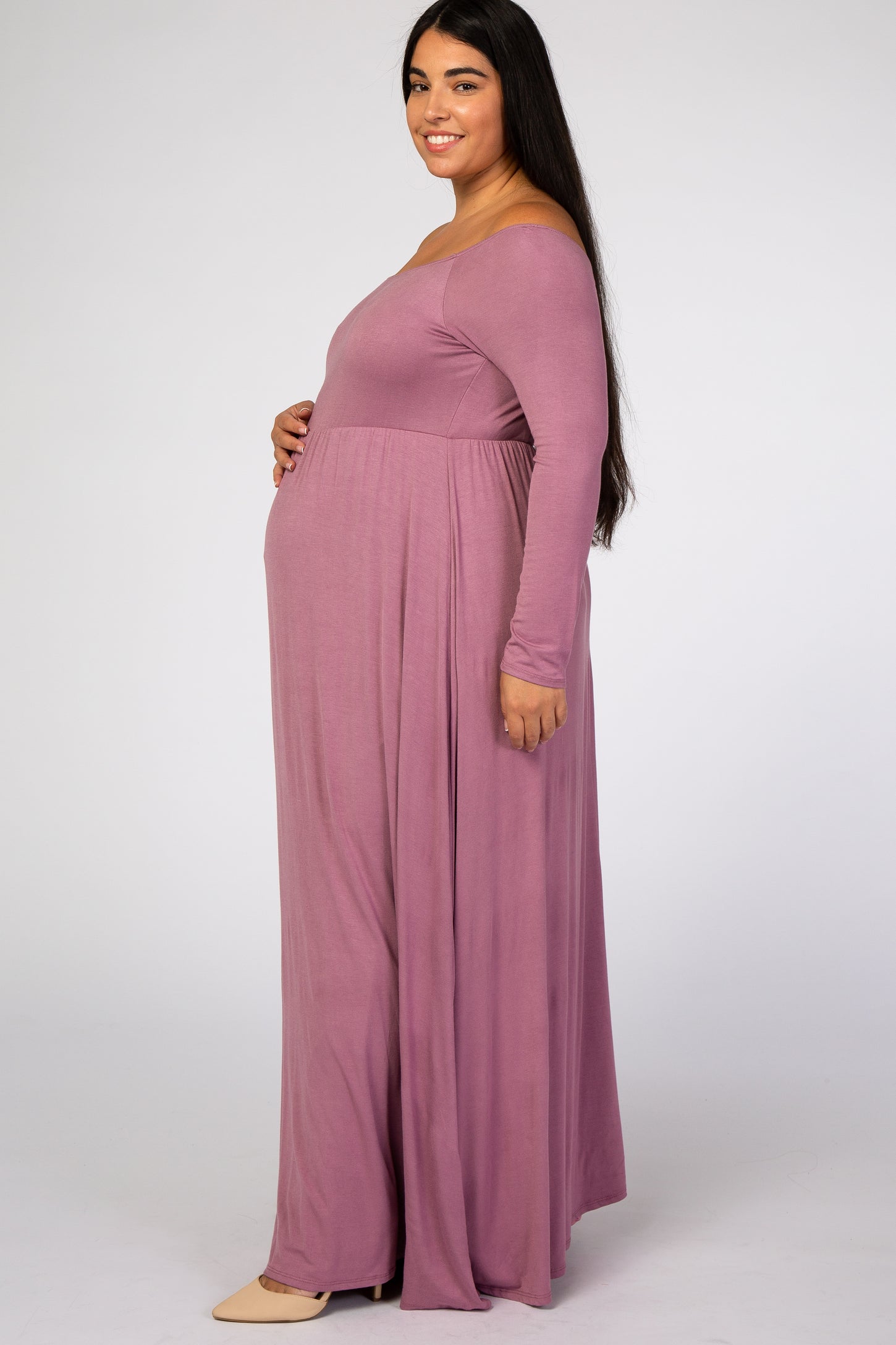 Pregnant woman in a long sleeve mauve maternity maxi dress posing against a white background
