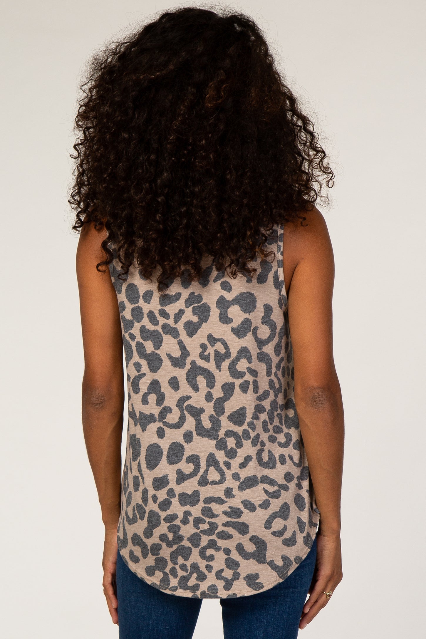 Back view of a woman with curly hair wearing a tan and grey leopard print tank top and blue jeans