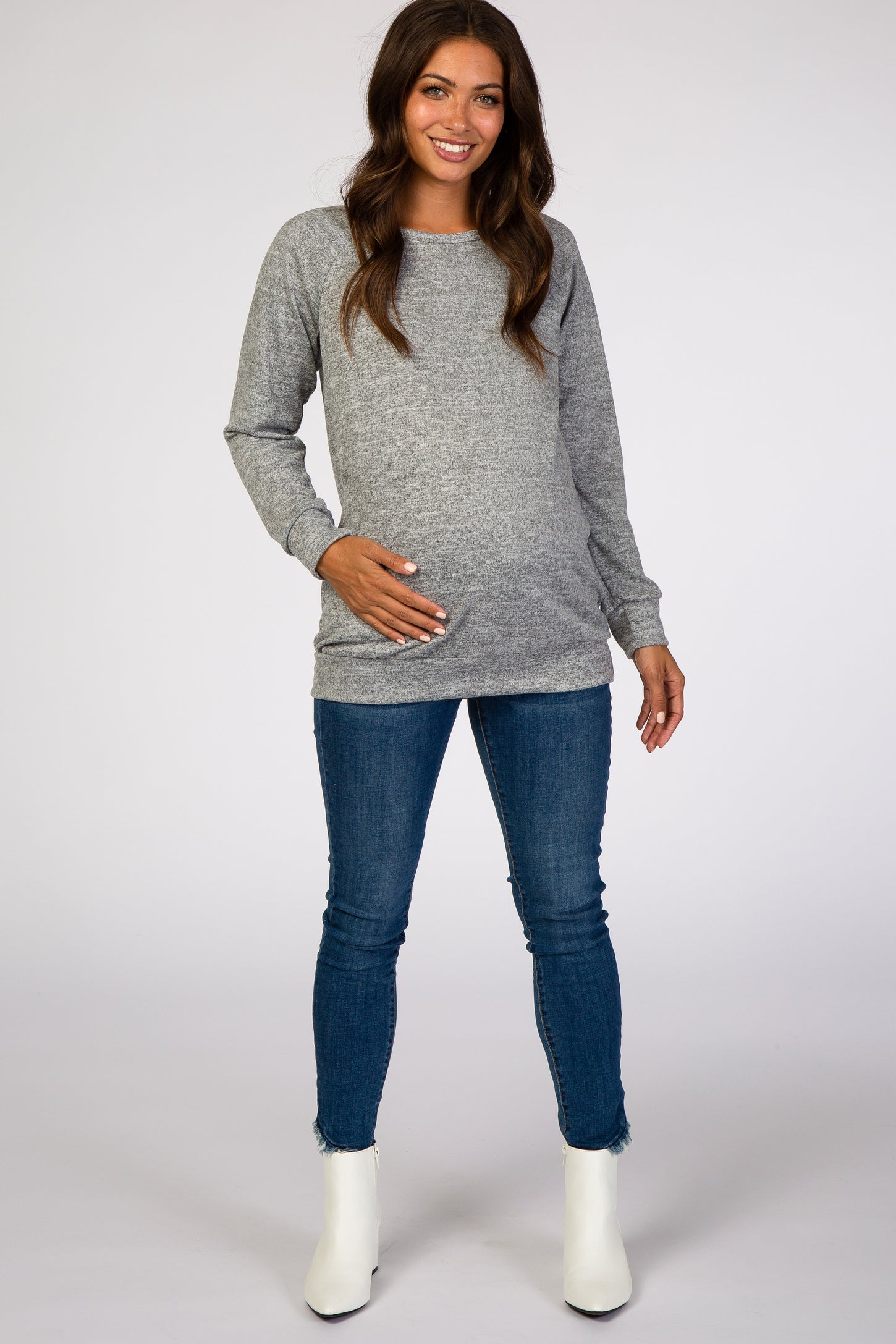 smiling pregnant woman wearing grey long sleeve maternity sweater and blue jeans with white boots