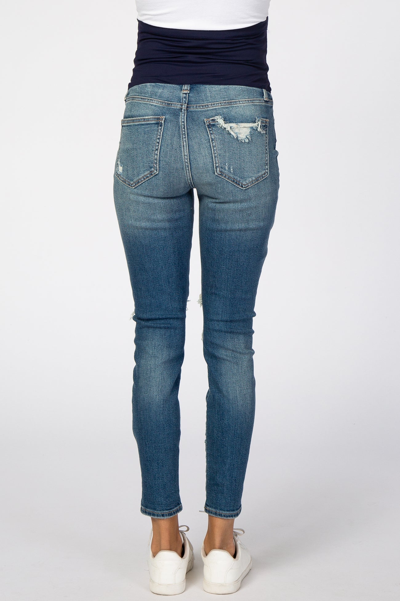 Rear view of woman wearing distressed blue skinny jeans with ripped back pocket and white sneakers