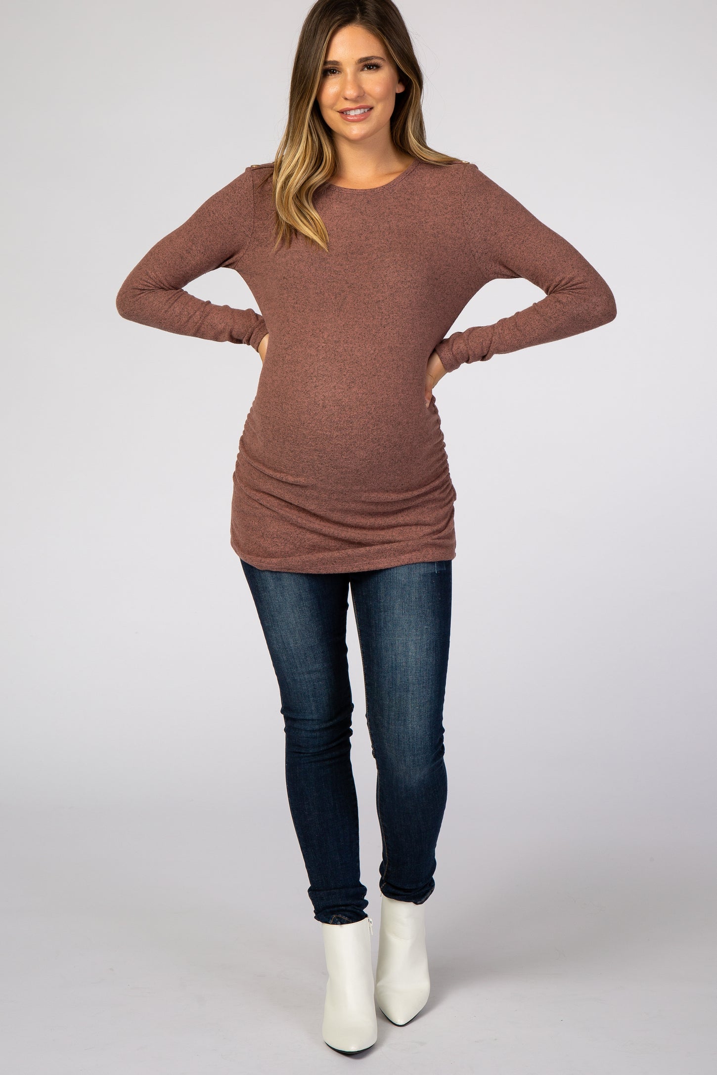 pregnant woman wearing a mauve long sleeve maternity tunic top and dark blue jeans with white boots