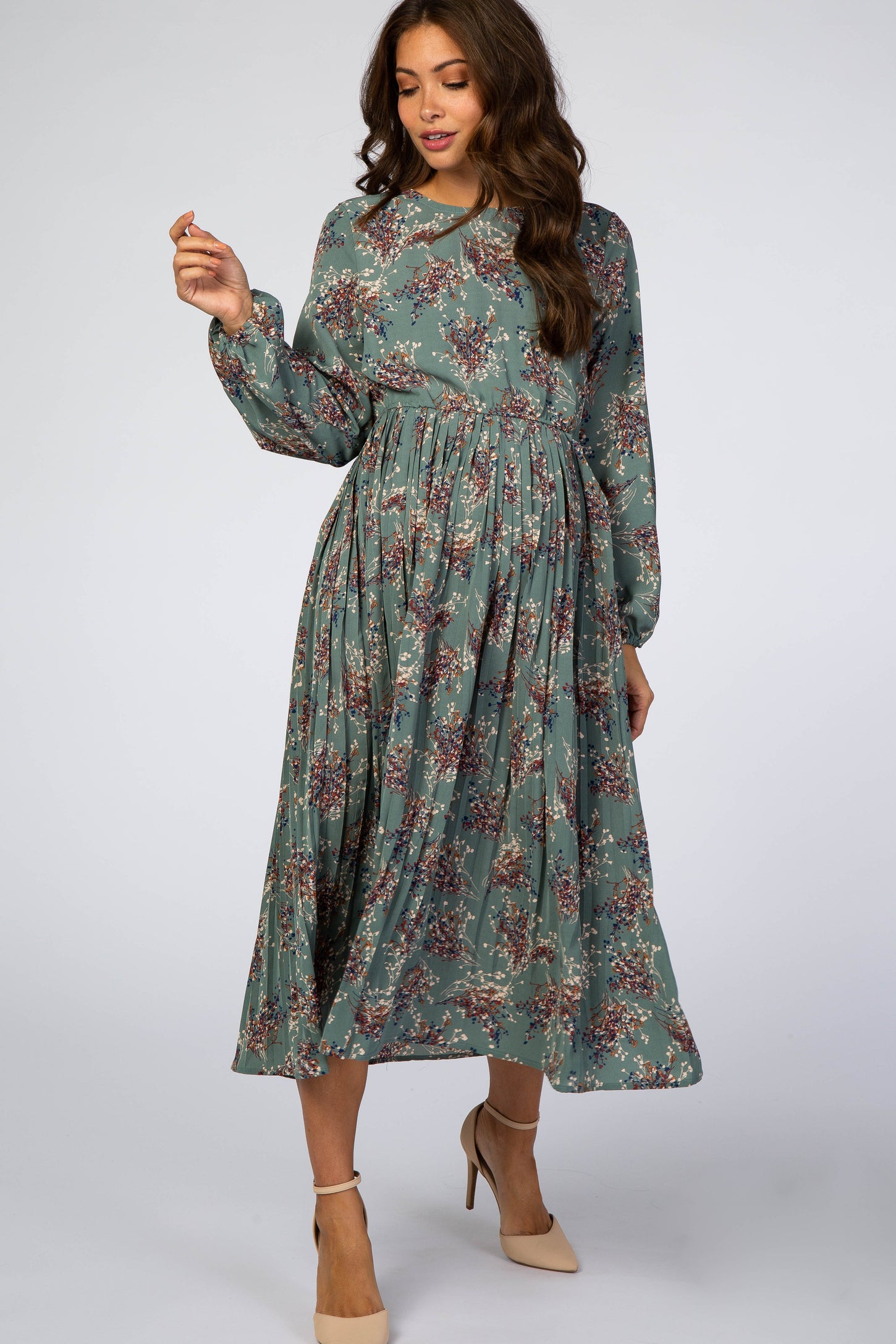 woman wearing a sage green floral long sleeve pleated maternity midi dress with beige heels
