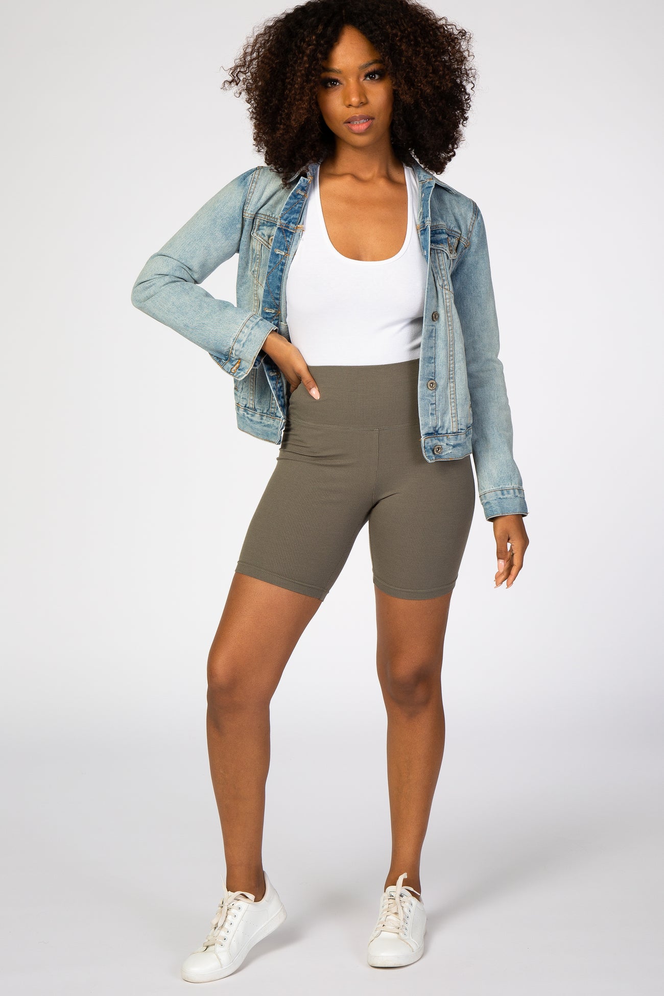 woman wearing olive green ribbed biker shorts with a white tank top and light wash denim jacket