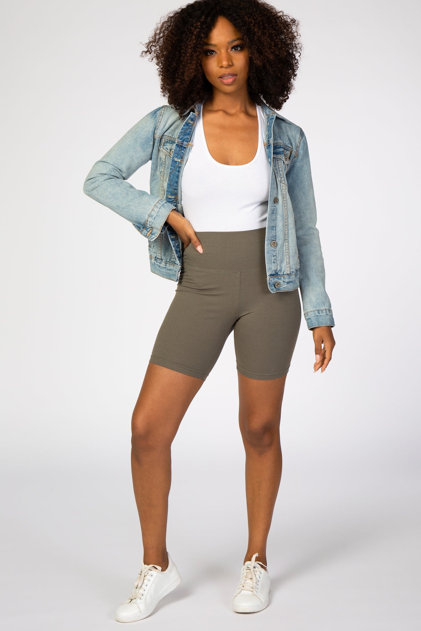 woman wearing olive green ribbed biker shorts with a white tank top and light wash denim jacket