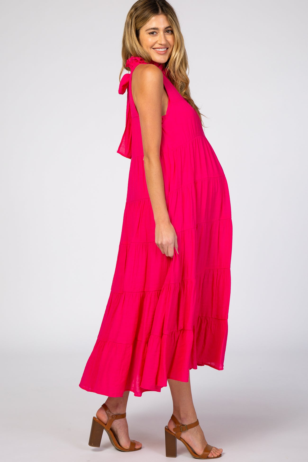 Pregnant woman wearing a hot pink tiered sleeveless maternity midi dress with brown block heel sandals
