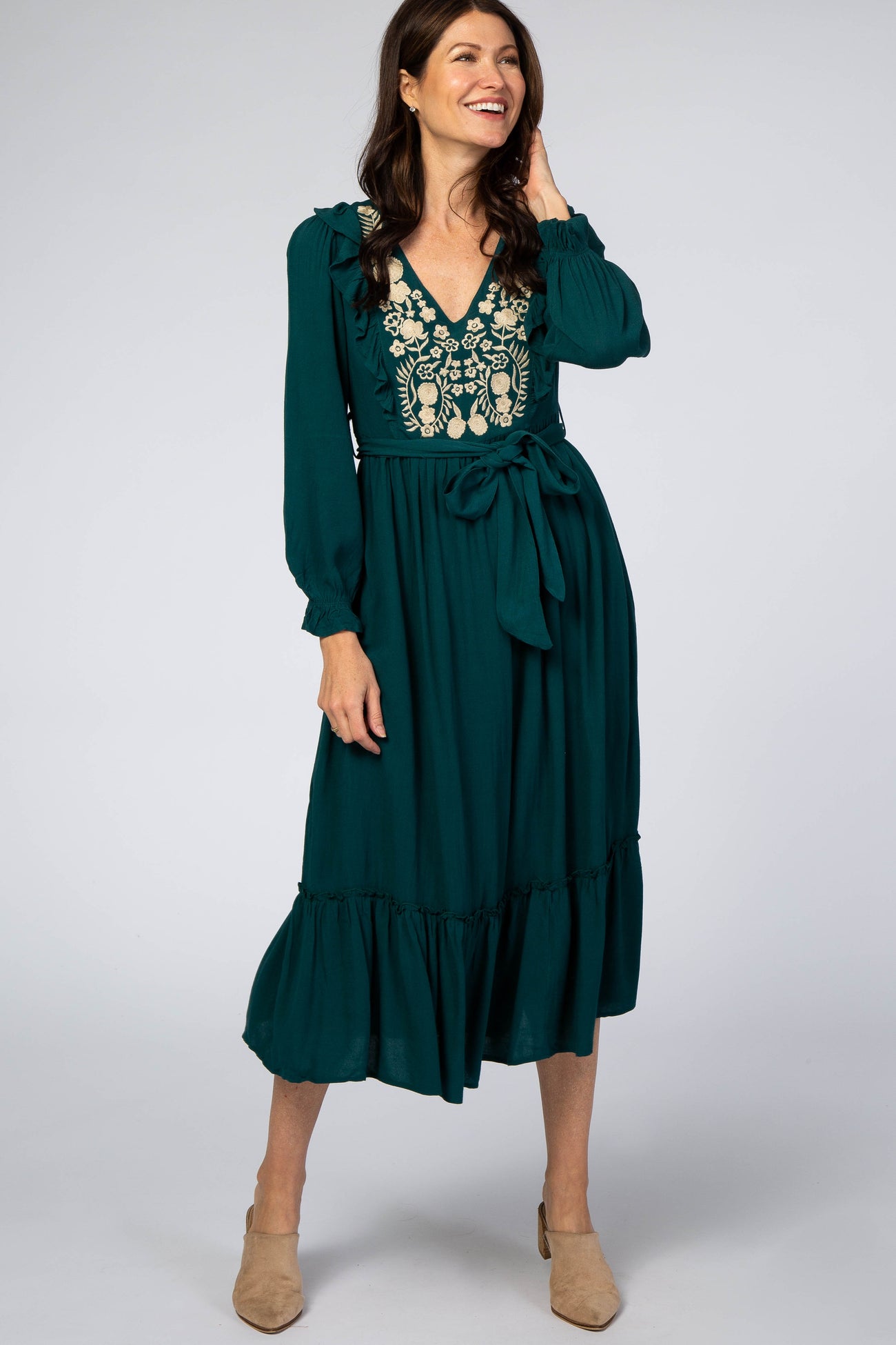 woman wearing a forest green long sleeve midi dress with floral embroidery and a waist tie