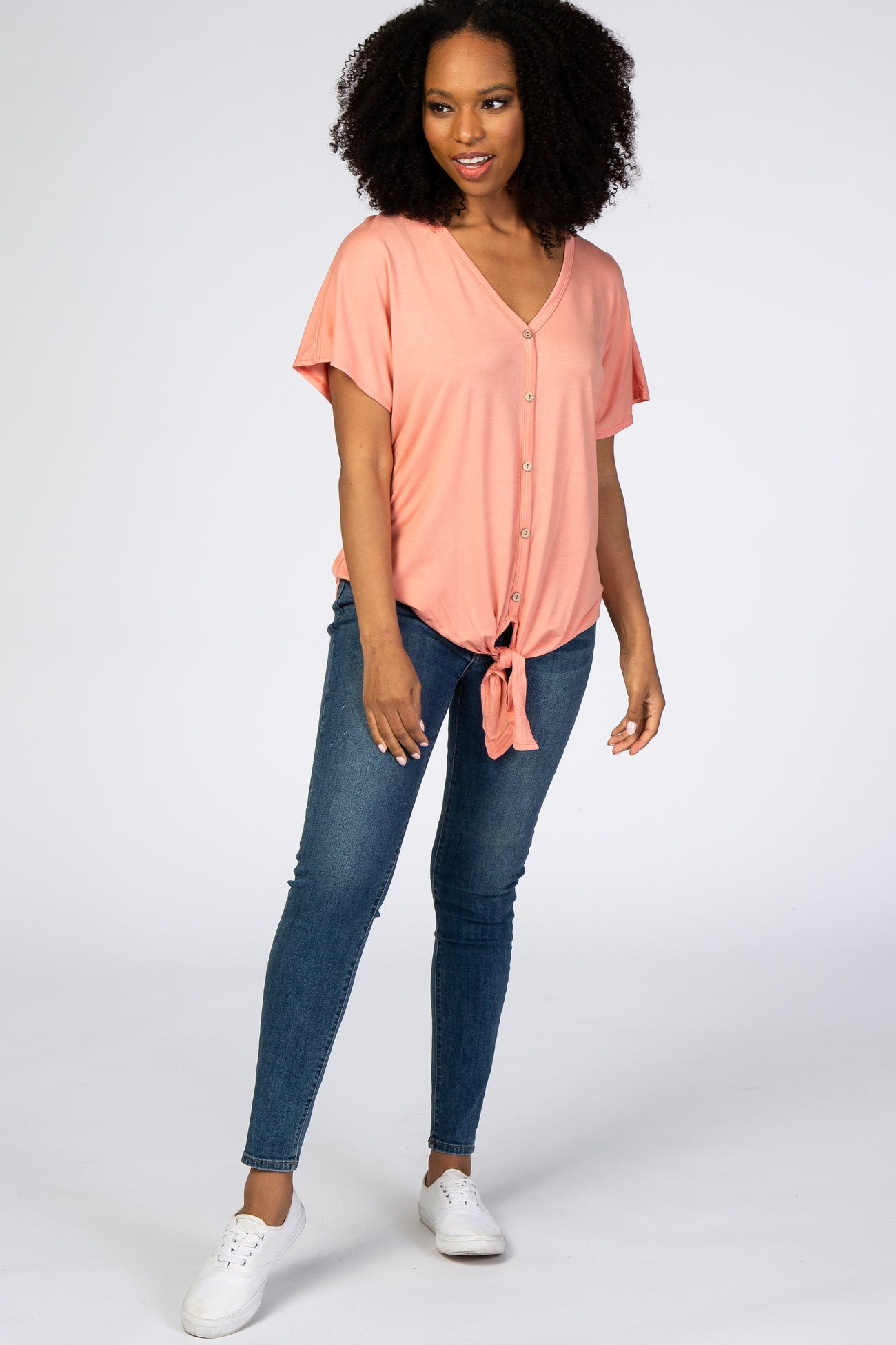 woman wearing peach short sleeve button down tie front top with blue skinny jeans and white sneakers