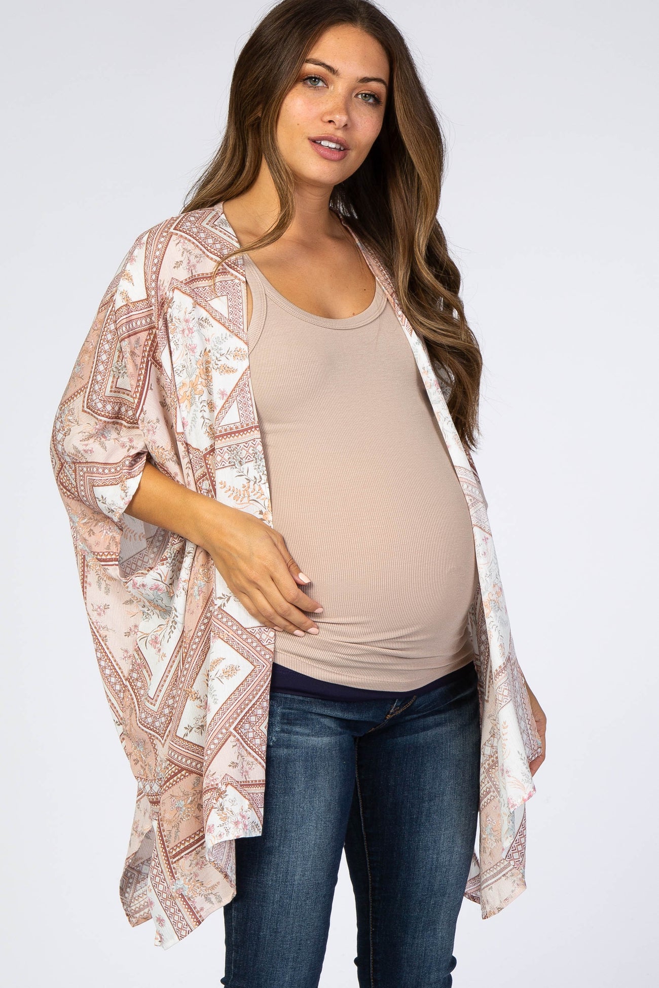 woman wearing a light pink patterned maternity kimono over a beige tank top and jeans, showcasing her baby bump