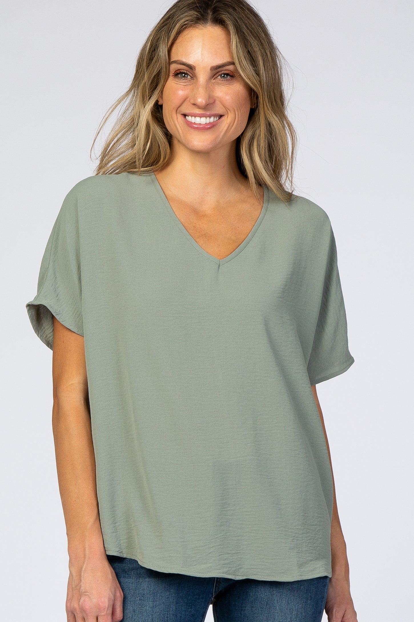 smiling woman wearing a sage green v-neck short sleeve blouse and blue jeans