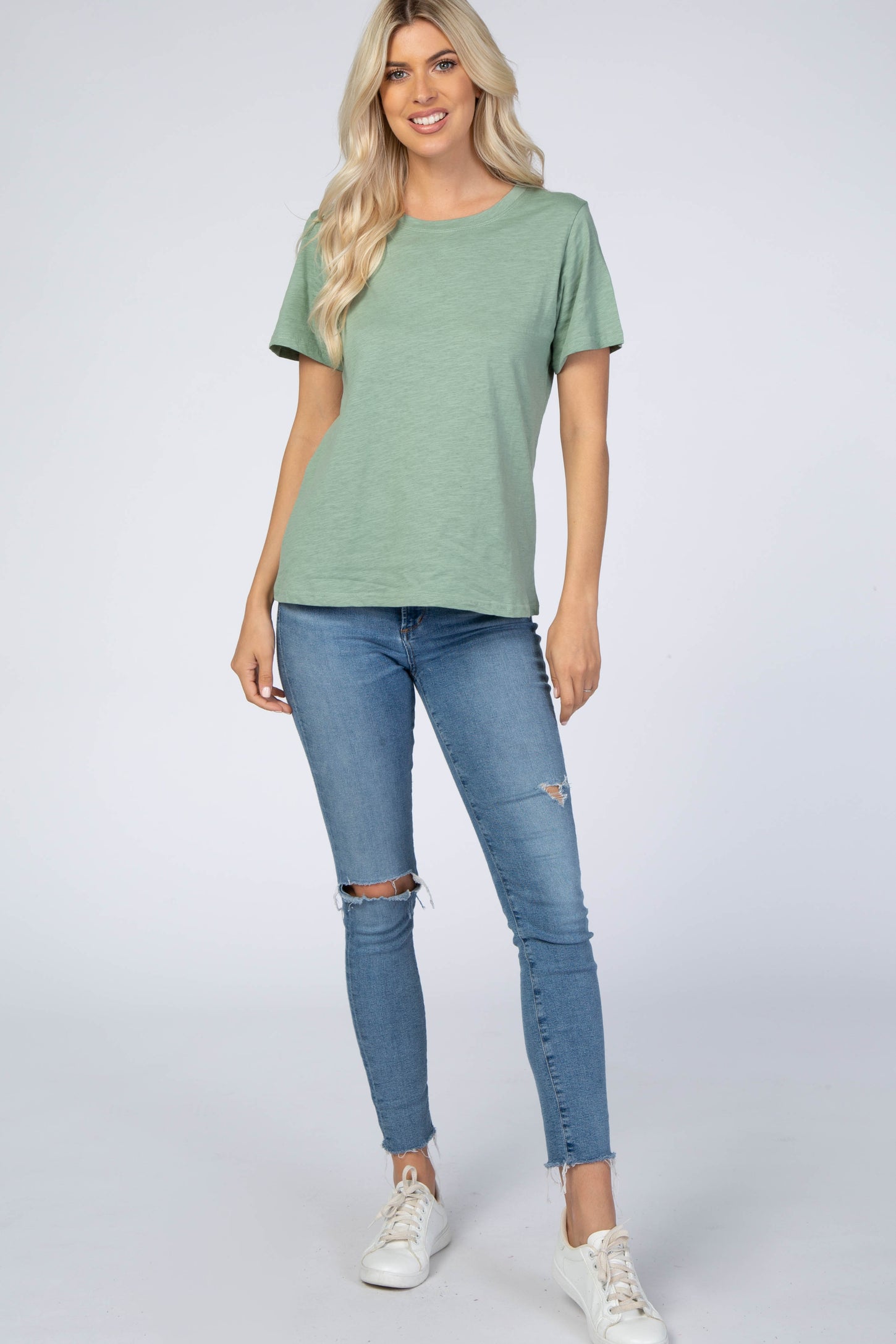 woman wearing a sage green short sleeve t-shirt and distressed blue skinny jeans with white sneakers