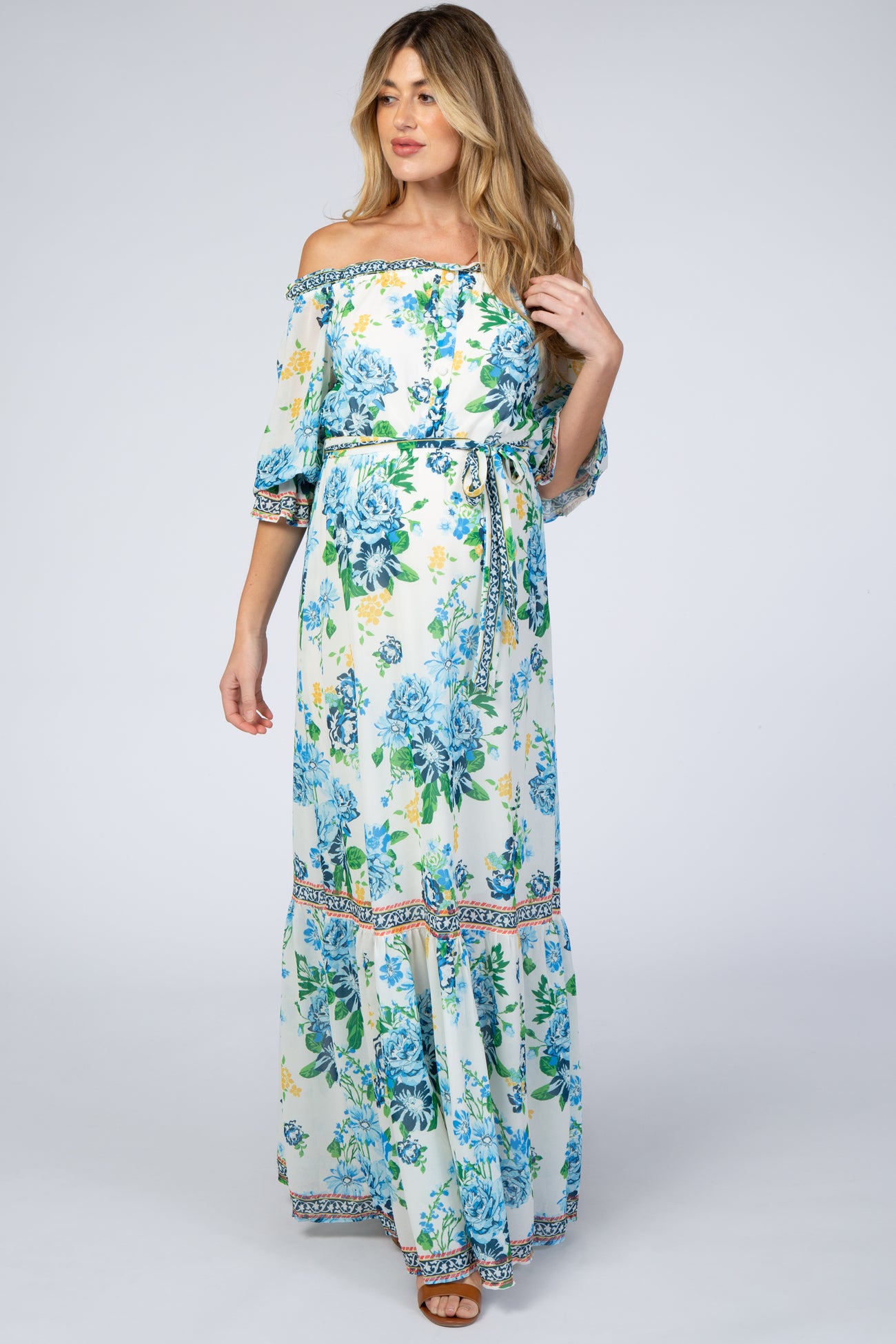 Pregnant woman wearing an off-the-shoulder white floral maternity maxi dress with blue and yellow flowers