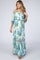 Pregnant woman wearing an off-the-shoulder white floral maternity maxi dress with blue and yellow flowers