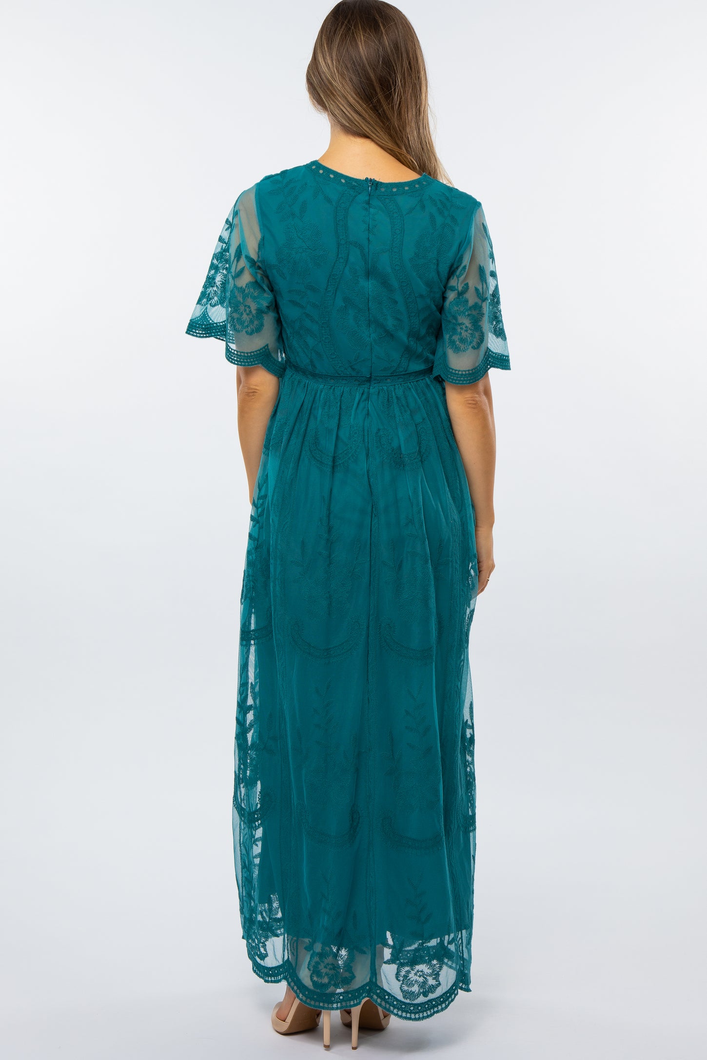 woman wearing a teal maternity maxi dress with short lace sleeves, showing the back view and flowing silhouette