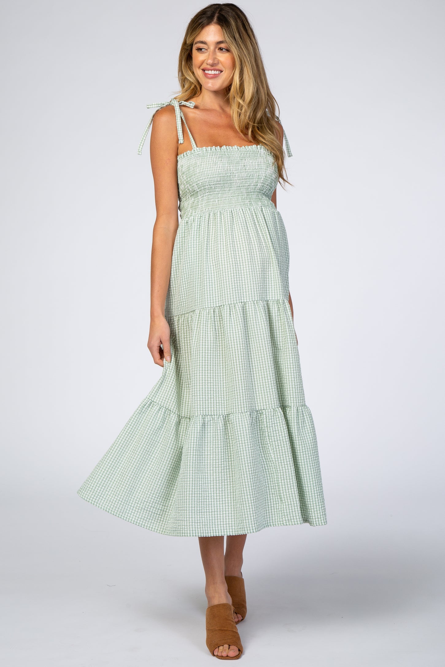 pregnant woman wearing a green and white gingham tiered maternity midi dress with tie straps